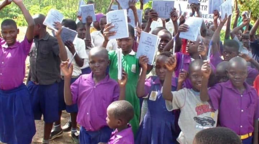 Children raising hands enthusiastically in a Ugandan classroom